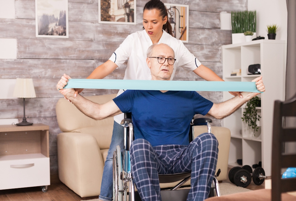 Woman helping a man in a wheelchair stretch a resistance band, as in occupational therapy for rheumatoid arthritis 